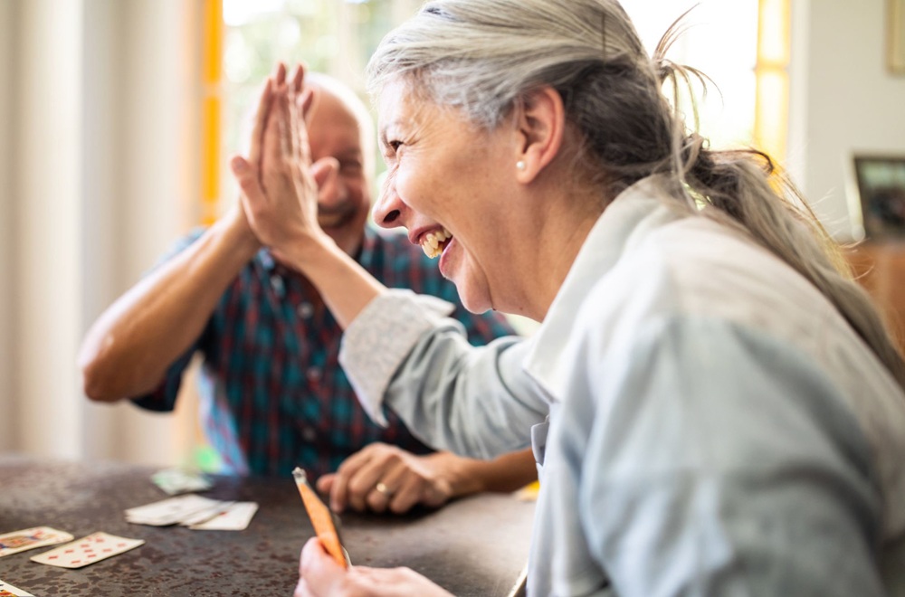 Argentinian elderly woman and man doing high-five during game with cards at home. ccrc model at senior living hospitality
