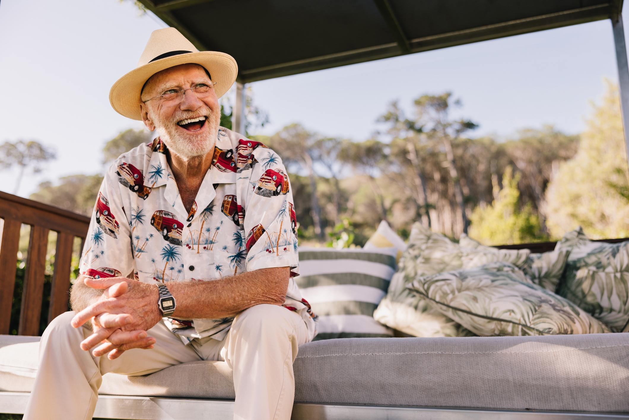 Vacationing after retirement. Happy elderly man laughing cheerfully while relaxing on a couch at a luxury spa resort. Carefree senior man enjoying himself while on a summer getaway - spring cleanup
