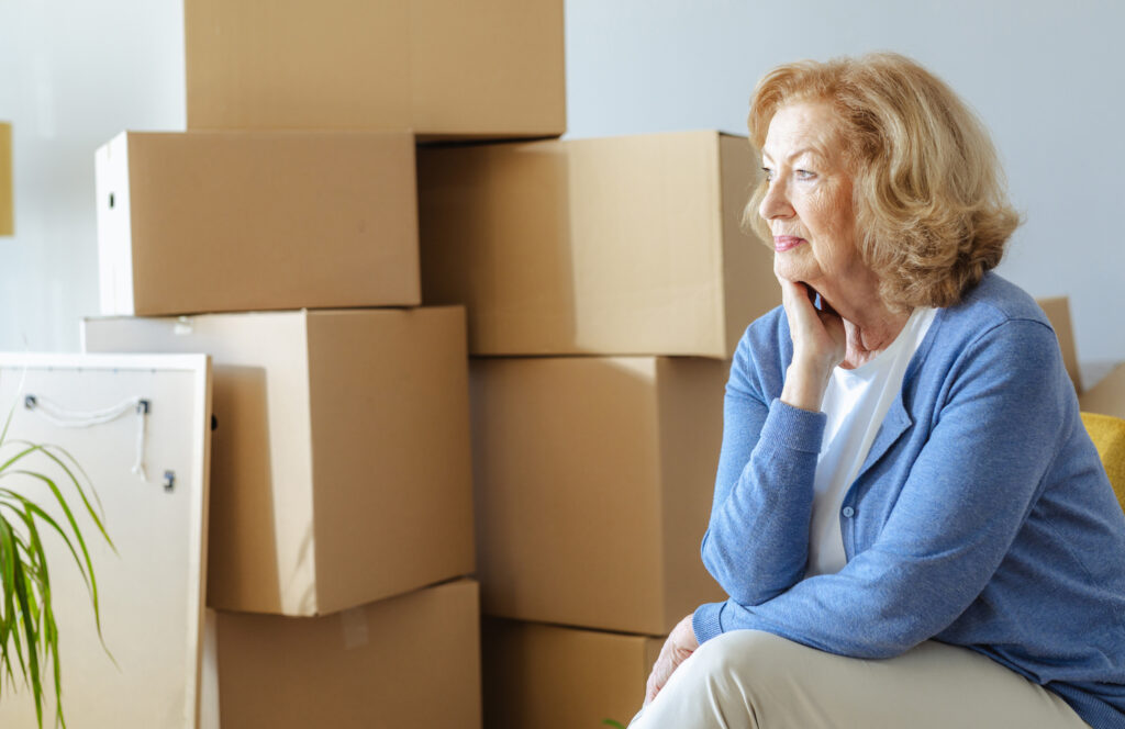 Senior woman sitting beside stacked moving boxes, thinking about the work of moving