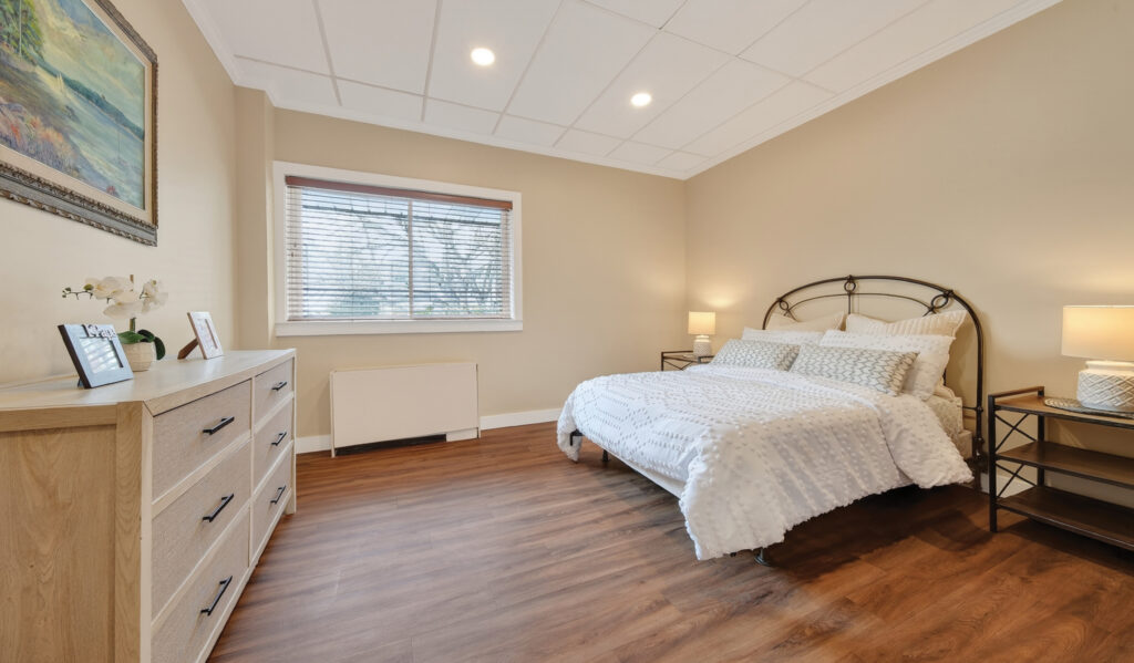Private suite bedroom at The Gardens at East Hill with warm wood floors and natural light