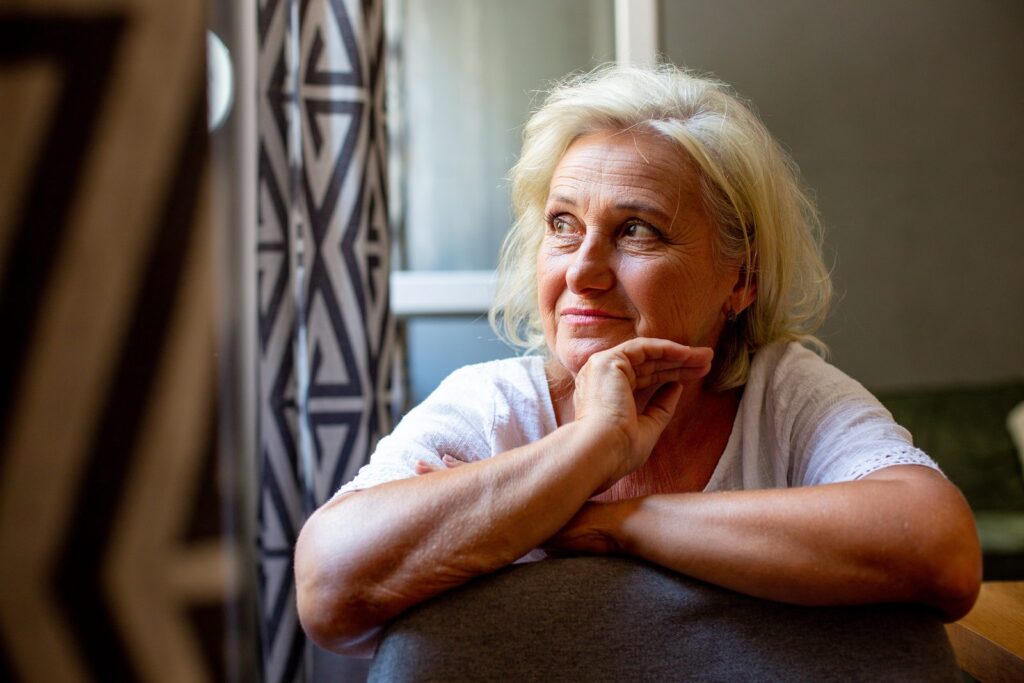 Senior woman gazing out a window, wondering whether staying in her home is still the right choice